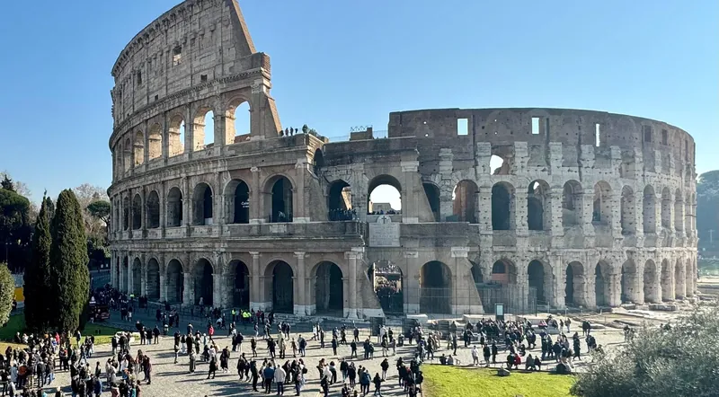 The Colosseum under a clear sky with visitors on the piazza