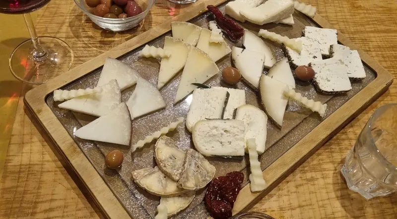A board of white and blue Lazio cheeses with honey and olives beside a glass of wine