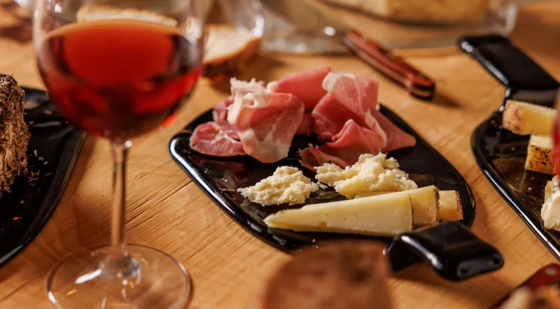 A glass of red Lazio wine beside a board of cured meats and cave-aged cheeses in Testaccio