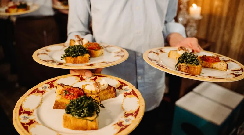 A waiter carrying plates of bruschetta with greens and tomatoes in a Roman trattoria