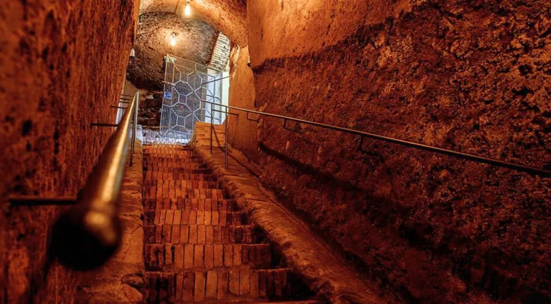 Stone steps descending into a lamp-lit underground cave in Rome