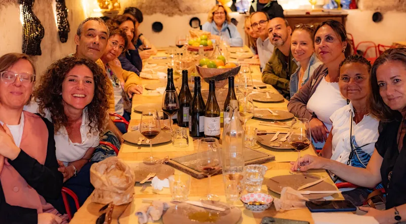 A long table of guests sharing wine, cheese and cured meats in the Testaccio cave