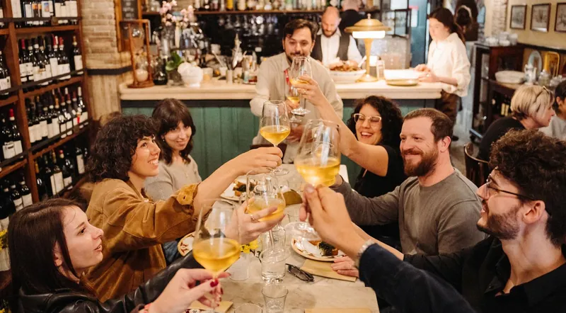 Friends raising glasses of white wine at a long table in a Trastevere osteria
