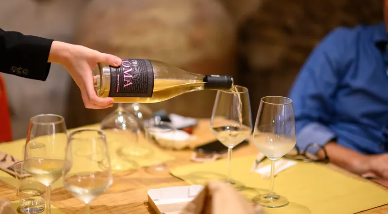 A host pouring white wine into tasting glasses on a candlelit table in Rome