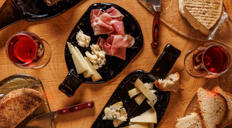 Overhead view of rose wine glasses, prosciutto and wedges of Lazio cheese on wooden boards