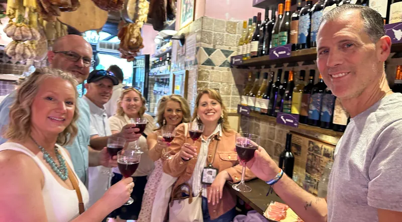 A food tour group raising glasses of red wine at a deli bar in Rome